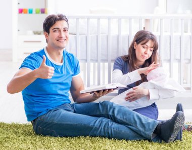 Yeni doğmuş bebekleriyle halıda oturan genç ebeveynler.