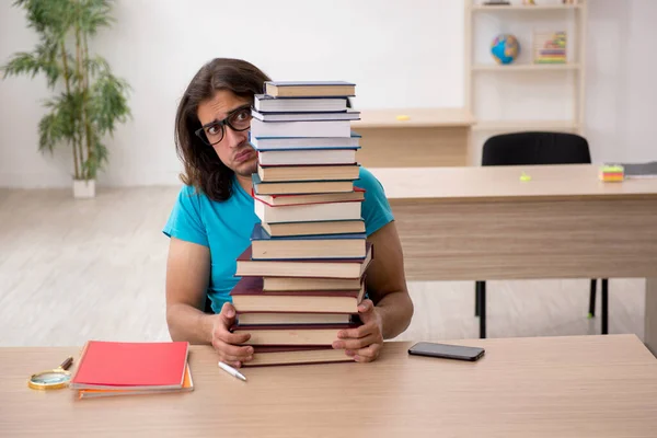 Jonge mannelijke student en veel boeken in de klas — Stockfoto