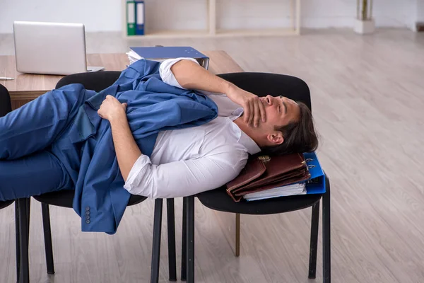 Jovem funcionário do sexo masculino dormindo no escritório em cadeiras — Fotografia de Stock