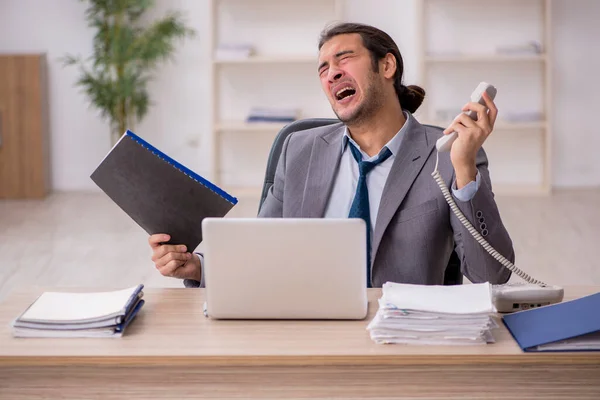 Jonge mannelijke werknemer ongelukkig met overmatig werk in het kantoor — Stockfoto