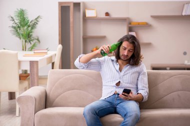 Genç adam evde alkol içiyor.