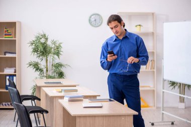 Genç erkek öğretmen ders sırasında elinde akıllı telefon tutuyor.