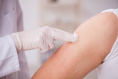 Genç erkek hasta yaşlı erkek doktoru aşıyla ziyaret ediyor.