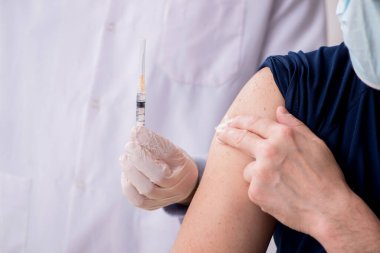 Yaşlı bir erkek hasta aşıyla genç bir doktoru ziyaret ediyor.