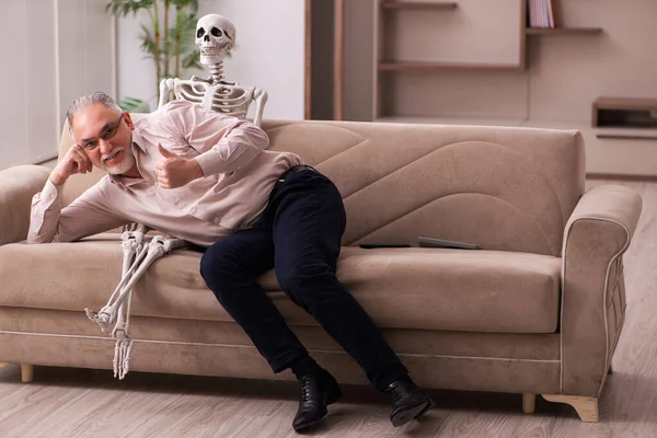 Velho sentado no sofá com o esqueleto feminino — Fotografia de Stock