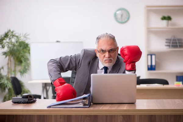 Alter Geschäftsmann mit Boxhandschuhen am Arbeitsplatz — Stockfoto