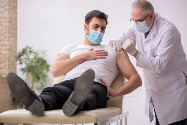 Ung manlig patient besöker gammal manlig läkare i vaccinationsgrupp — Stockfoto