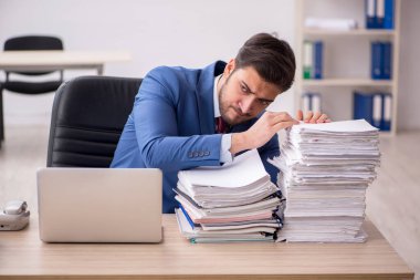 Genç bir erkek çalışan ve ofiste çok fazla iş var.