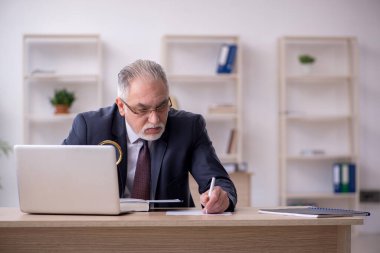 Eski erkek çalışan işyerinde oturuyor.