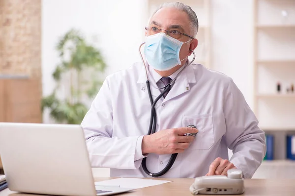 Yaşlı erkek doktor salgın sırasında klinikte çalışıyor. — Stok fotoğraf