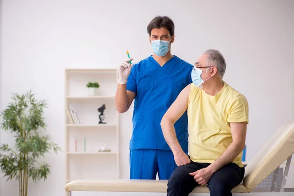 Old male patient visting young male doctor in vaccination concep — Stock Photo, Image