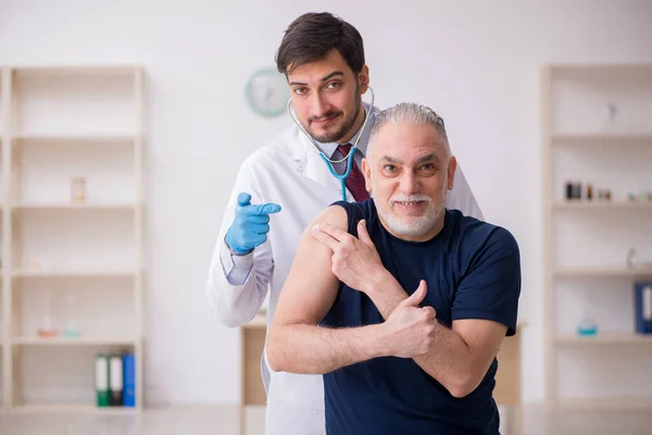 Oude mannelijke patiënt op bezoek bij jonge mannelijke arts in vaccinatiecentrum — Stockfoto