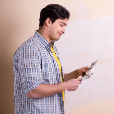 Evdeki duvara alçı yapıştıran genç adam.