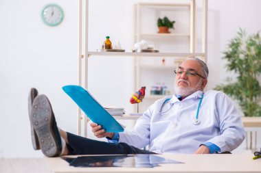 Yaşlı erkek doktor klinikte not alıyor.