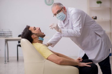 Genç erkek hasta yaşlı doktor otorhinolaryngologis 'i ziyaret ediyor.