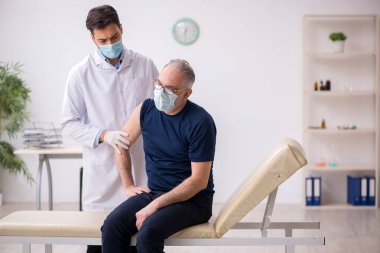 Yaşlı bir erkek hasta aşıyla genç bir doktoru ziyaret ediyor.