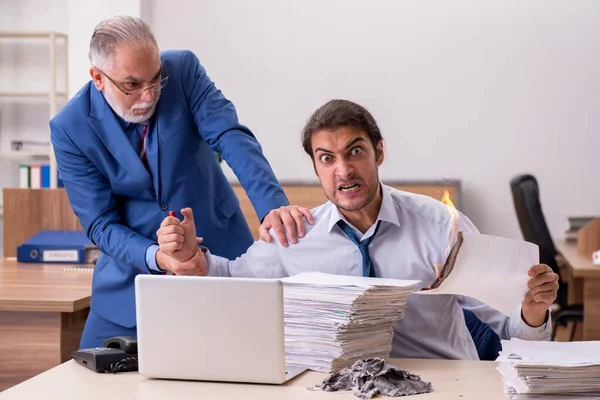 Young male employee and old boss burning papers at workplace — Stock Photo, Image