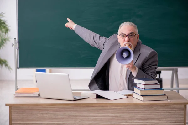 Velho professor do sexo masculino segurando megafone na frente de quadro negro — Fotografia de Stock