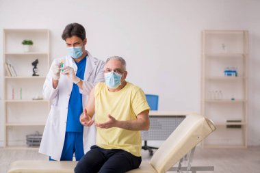 Yaşlı erkek hasta aşılama bölümünde genç bir erkek doktor.