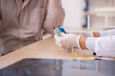 Yaşlı bir erkek hasta aşıyla genç bir doktoru ziyaret ediyor.