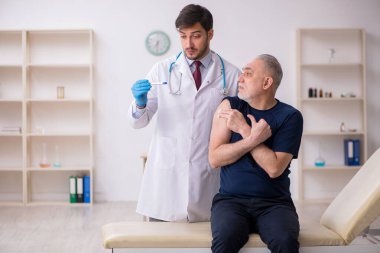 Yaşlı bir erkek hasta aşıyla genç bir doktoru ziyaret ediyor.