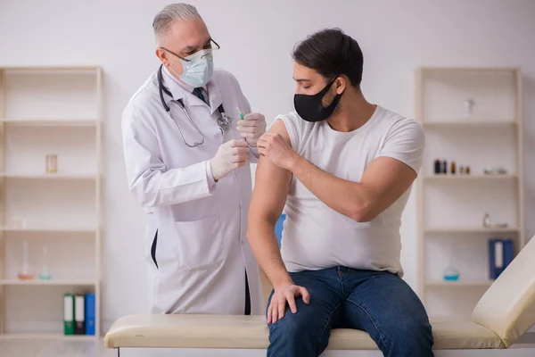 Junge männliche Patienten besuchen alten Arzt im Impfkonzept — Stockfoto