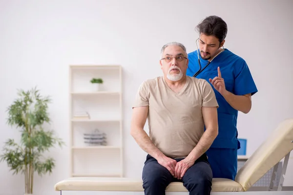 Starý muž pacient visting mladý muž lékař — Stock fotografie