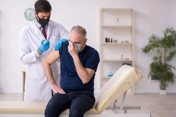 Oude mannelijke patiënt op bezoek bij jonge mannelijke arts in vaccinatiecentrum — Stockfoto