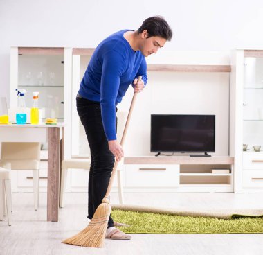 Genç adam yerleri süpürgeyle temizliyor.