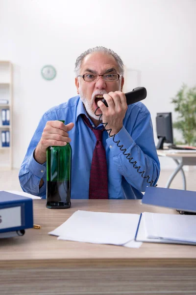 Starý muž zaměstnanec pití alkoholu v kanceláři — Stock fotografie