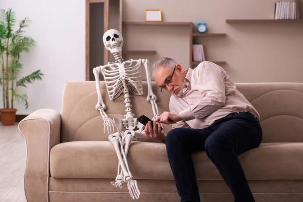 Old man sitting on the sofa with the female skeleton — Stock Photo, Image