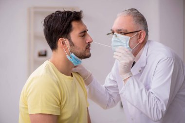 Genç erkek hasta yaşlı doktor otorhinolaryngologis 'i ziyaret ediyor.