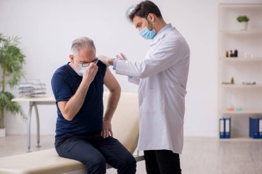 Yaşlı bir erkek hasta aşıyla genç bir doktoru ziyaret ediyor.