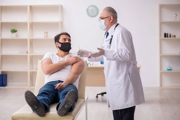 Junge männliche Patienten besuchen alten Arzt im Impfkonzept — Stockfoto