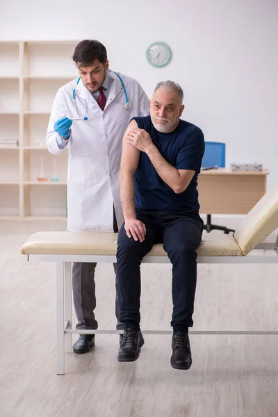 Oude mannelijke patiënt op bezoek bij jonge mannelijke arts in vaccinatiecentrum — Stockfoto