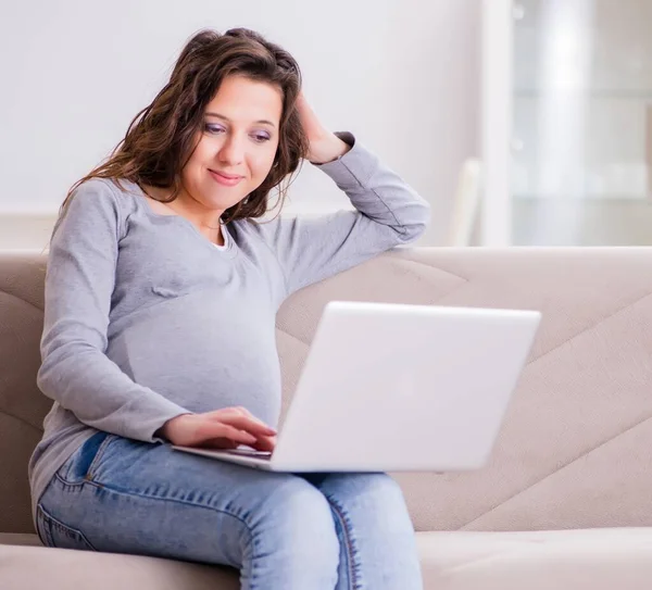 Schwangere arbeitet am Laptop und sitzt auf Sofa — Stockfoto