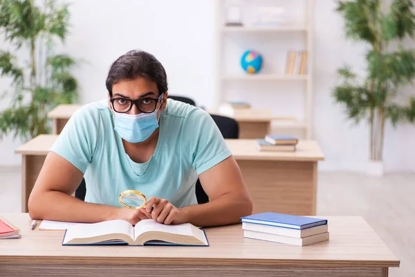 Giovane studente maschio seduto in classe indossando maschera — Foto Stock