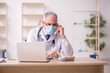 Yaşlı erkek doktor salgın sırasında klinikte çalışıyor.