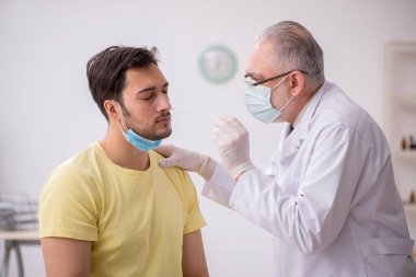 Genç erkek hasta yaşlı doktor otorhinolaryngologis 'i ziyaret ediyor.