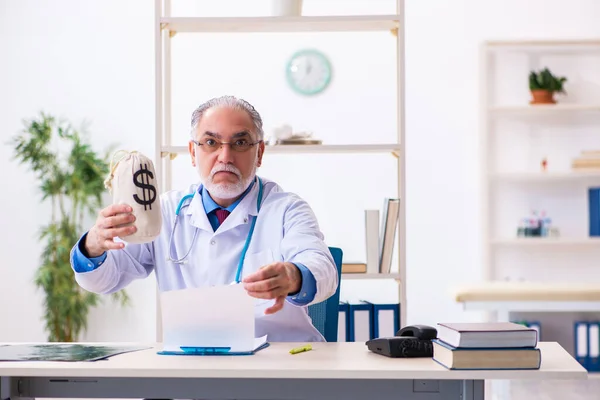 Velho médico masculino segurando saco de dinheiro no hospital — Fotografia de Stock