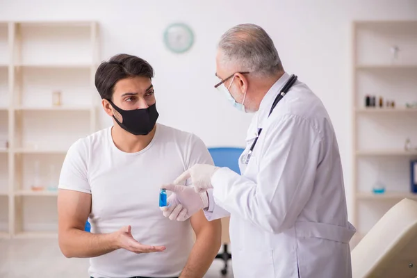 Junge männliche Patienten besuchen alten Arzt im Impfkonzept — Stockfoto