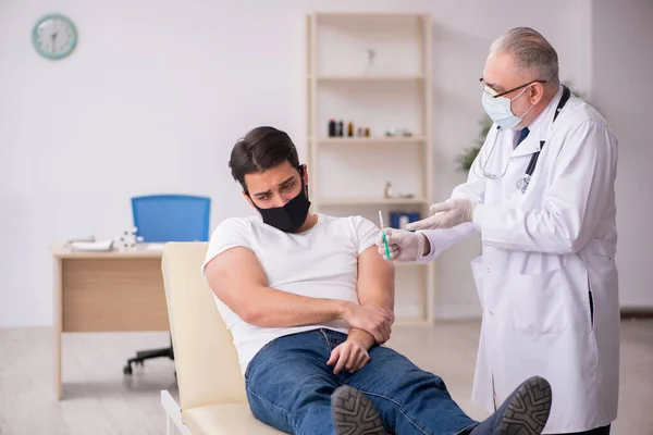 Junge männliche Patienten besuchen alten Arzt im Impfkonzept — Stockfoto