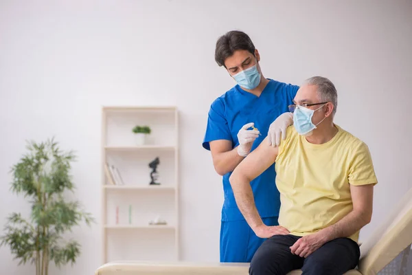 Starý muž pacient visting mladý muž lékař v vakcinaci konjunktura — Stock fotografie