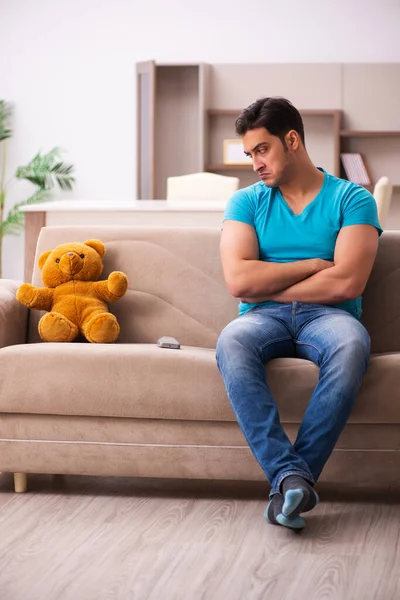 Młody mężczyzna siedzi z niedźwiedzią zabawką w domu — Zdjęcie stockowe