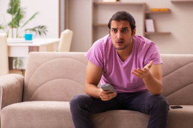 Genç adam salgın sırasında evde televizyon izliyor.