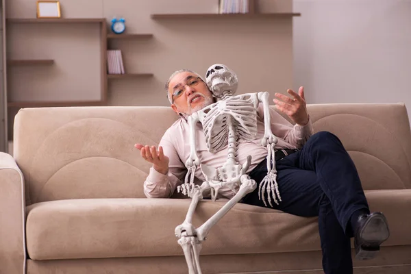 Alter Mann sitzt auf dem Sofa mit dem weiblichen Skelett — Stockfoto