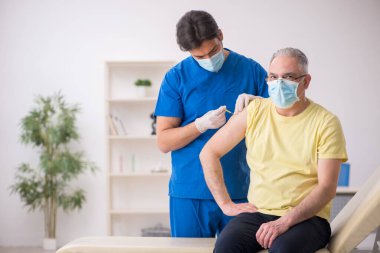 Yaşlı erkek hasta aşılama bölümünde genç bir erkek doktor.