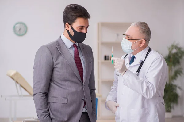 Genç işadamı aşı danışmanıyla yaşlı doktoru ziyaret ediyor. — Stok fotoğraf