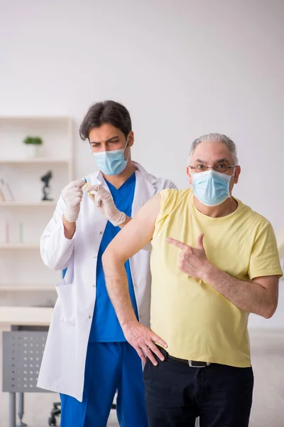 Alte männliche Patientin besucht junge männliche Ärztin bei Impfung — Stockfoto