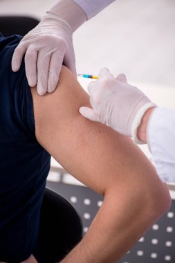 Genç erkek hasta yaşlı erkek doktoru aşıyla ziyaret ediyor.